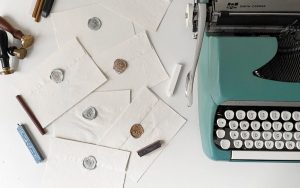 Vintage mint typewriter beside sealed handmade envelopes and wax seals arranged on a white surface.