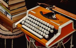 Orange vintage typewriter placed beside a stack of books in a warm, softly lit interior.